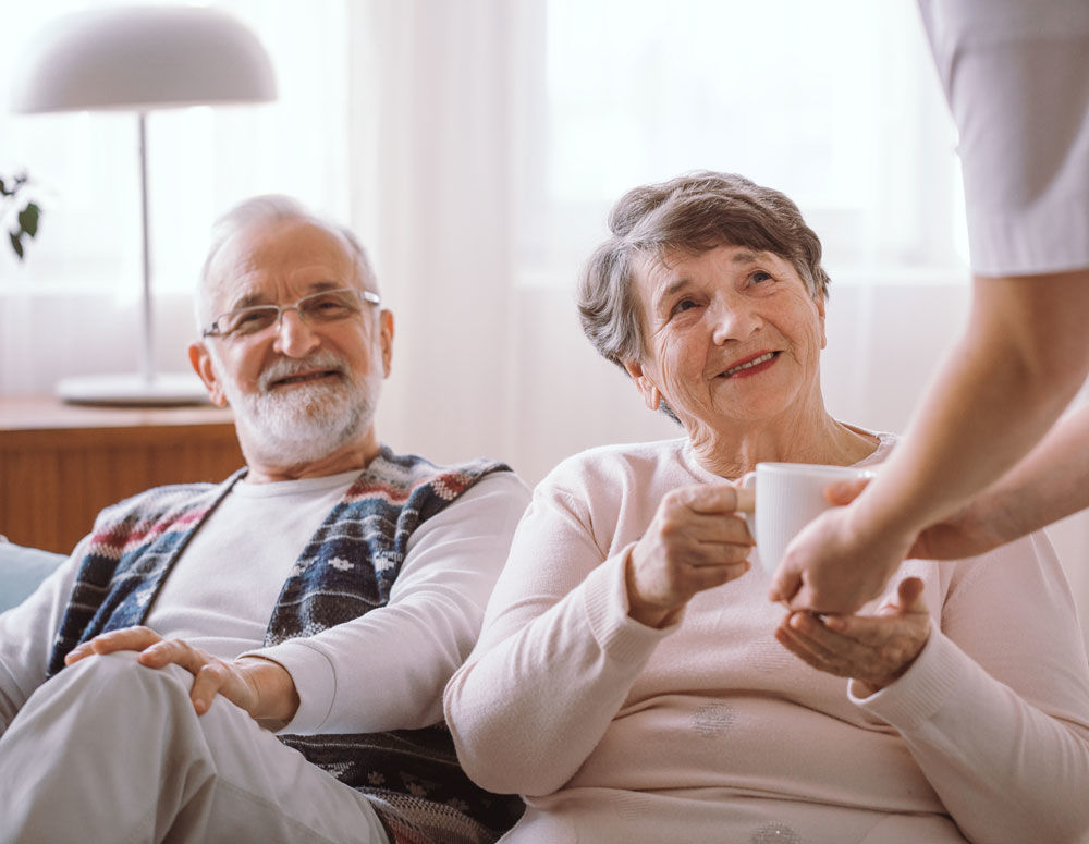 Elderly man and woman being handed a cup of tea