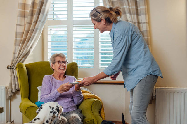 Carer giving elderly lady a plate of food.